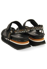 Sandalias negras con una correa trenzada, presentando una suela gruesa multicolor con capas en naranja, blanco y negro. Plantilla texturizada para mayor comodidad.