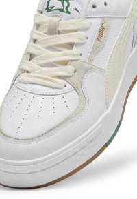 Białe sneakersy z teksturowanej skóry i zamszowymi akcentami. Charakteryzują się sznurowaniem, perforowaną budą na palce, gumową podeszwą oraz zielonymi detalami. 