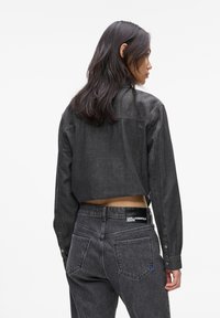 Crna denim kratka košulja s dugmadi na manžetama, uparena s crnim trapericama visokog struka koje imaju zakrpu s logom i stražnje džepove. Glatka tekstura.