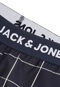 Marineblauwe boxershort met een wit ruitpatroon en een elastische tailleband met "JACK & JONES" in vetgedrukte witte letters.