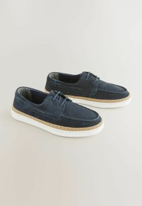 Laivastonsiniset nubukistä tekemät slip-on-kengät, joissa on valkoiset kumipohjat ja juuttiköysiä reunassa, ja yksinkertainen nauhateko.