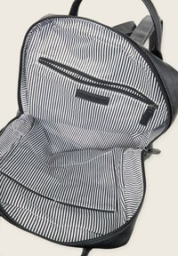 Wnętrze black skórzanskiej plecaka z białą i czarną paskowaną podszewką, kieszenią na zamek oraz dodatkowymi kieszeniami wsuwanymi po bokach.