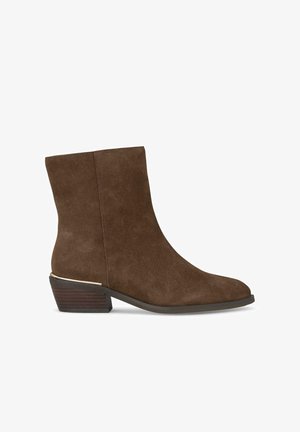 Bottine en suède marron avec un bout arrondi et un petit talon empilé, dotée d'un accent métallique à la base du talon. Texture lisse, design minimaliste.