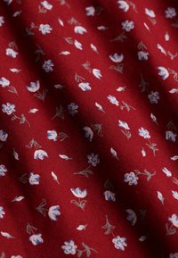 Rødt stof med lille hvidt og blåt blomsterprint, der viser tekstur og bløde folder.