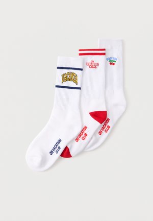 Trys balti laivo stiliaus kojinai su skirtingais dizainais: „VACANZA“ su mėlynomis juostelėmis, „ON VACATION Club“ su raudonais akcentais ir „DOLCE VITA“ su vyšnios grafika.