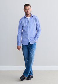 Svijetloplava i bijela prugasta košulja na kopčanje s dugim rukavima, uparena s plavim trapericama i crnim cipelama s crvenim akcentima.