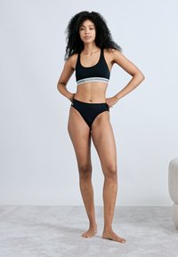Μαύρο αθλητικό σετ μπικίνι με κορυφή cropped και ριγέ λωρίδα στη βάση, εσώρουχα με ψηλή μέση, λείο ύφασμα και ελάχιστες λεπτομέρειες.