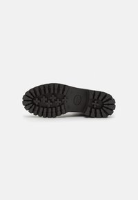 Suela de bota de goma negra con profundos surcos y patrones en forma de flor, diseñada para tracción y durabilidad.