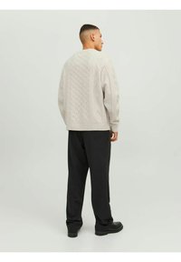 Light gray knitted sweater with textured cable patterns, round neckline, and a relaxed fit, paired with dark, loose-fitting trousers.