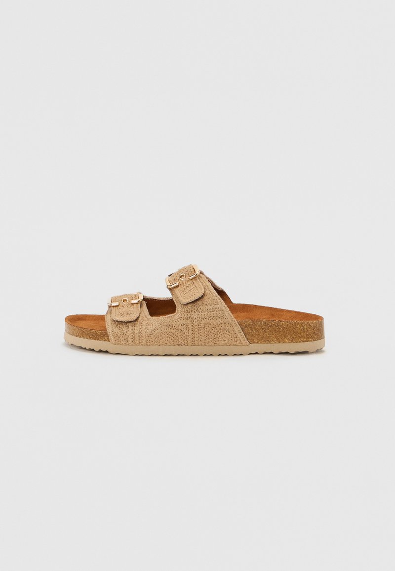 Sandale slide din suede bej, cu două curele reglabile cu catarame aurii, un suport din plută și un material texturat. Talpă plată cu un ușor profil.