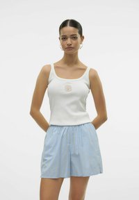 Witte geribde tanktop met een schelpenborduursel in het midden, gecombineerd met lichtblauwe gestreepte shorts met een elastische tailleband.