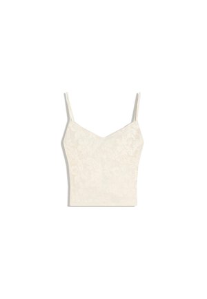 Camisole courte couleur crème avec fines bretelles et motif floral subtil sur fond clair.