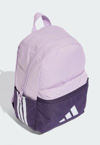 Sac à dos en tissu violet en forme ronde, avec une poche zippée à l'avant, trois rayures blanches et un logo blanc en bas.