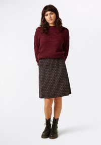 Burgundy neulepaita, kuvioitu musta hame kukkakuviolla ja mustat nauhakiinnitteiset taistelukengät. Rakenteelliset materiaalit; istuva ja liehukammioinen muotoilu.
