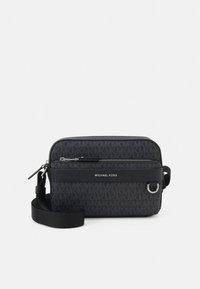 Czarna materiałowa torba na ramię z teksturowanym wzorem logo, przednią kieszenią na zamek, skórzanymi akcentami oraz regulowanym paskiem. Srebrne elementy metalowe.