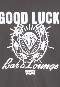 Gray fabric features white graphic text reading "GOOD LUCK" with a diamond design surrounded by rays and additional accents. Levi's logo present.