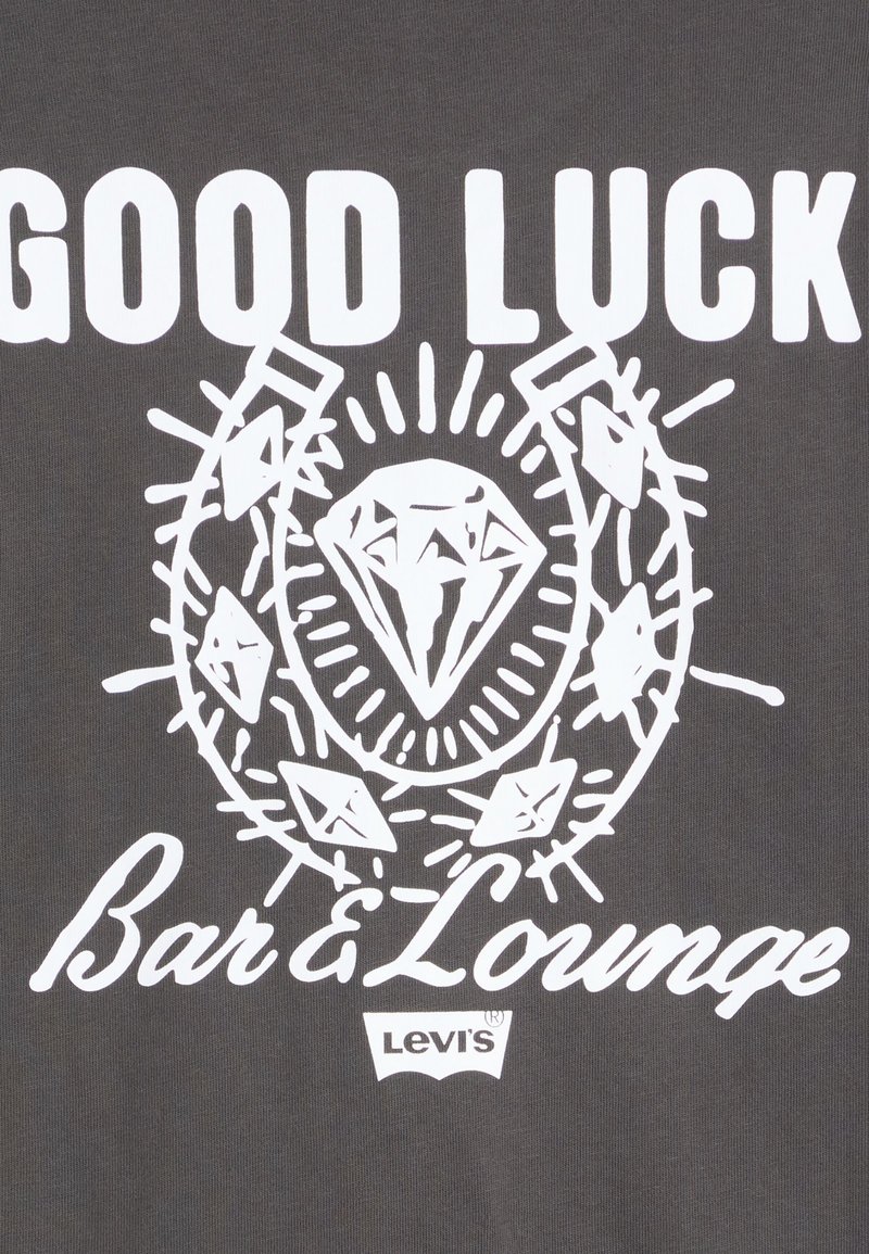 Grau Stoff mit weißem grafischen Text "Viel Glück", umgeben von einem Diamantdesign und Strahlen sowie zusätzlichen Akzenten. Levi's Logo vorhanden.