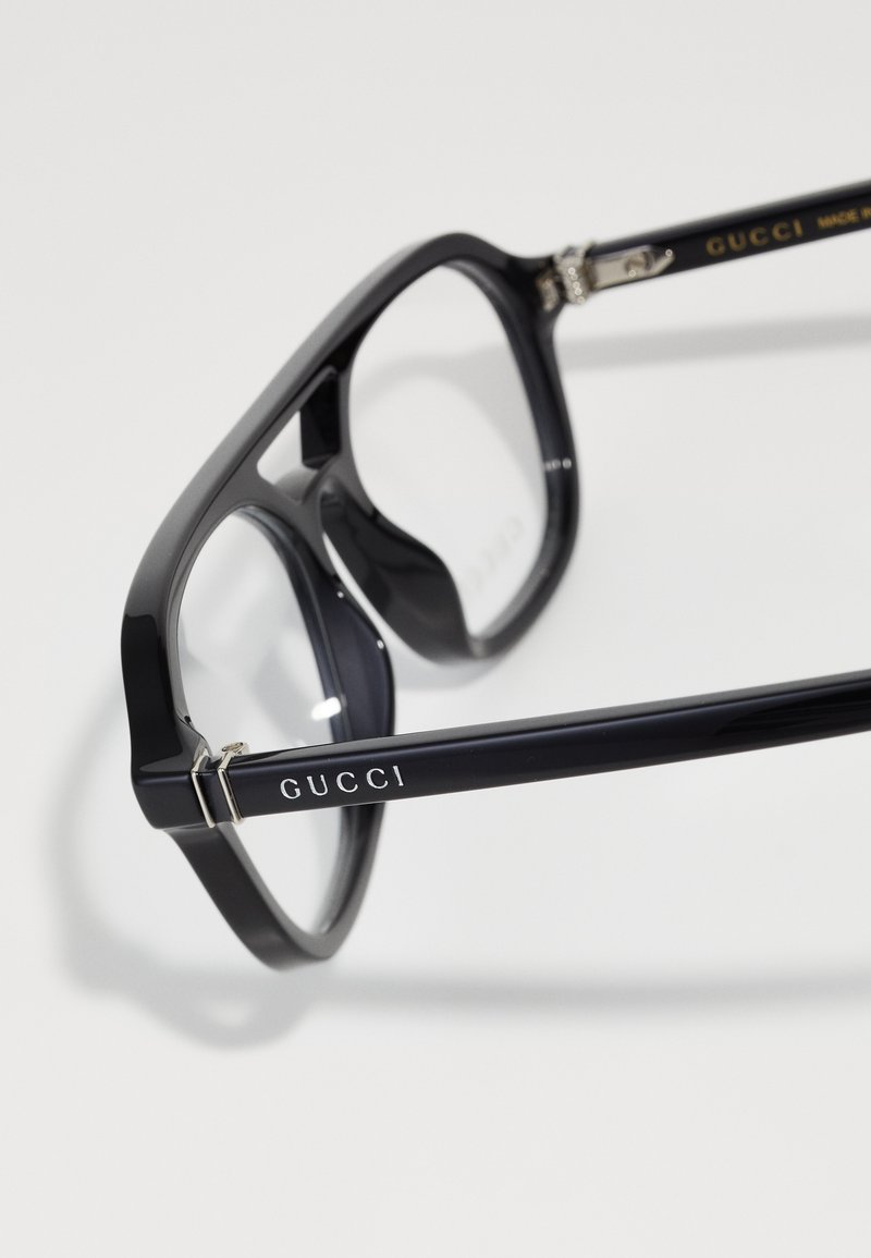 Zwarte rechthoekige Gucci-zonnebril met een glanzende afwerking, voorzien van heldere lenzen en een subtiel logo op de poot. Inclusief metalen scharnieraccenten.