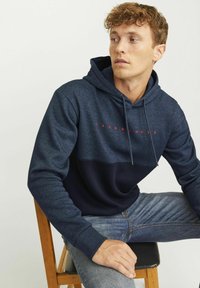 Sudadera con capucha en color marino con un diseño de bloques de color, que presenta una parte superior en azul claro y una parte inferior en azul oscuro, con texto de logo en rojo. Tela de mezcla de algodón.