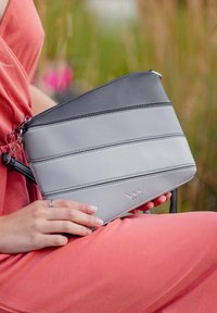 Šedá a černá crossbody taška s horizontálním pruhovaným designem, vyrobená z umělé kůže, s stříbrným zipem a logem značky.