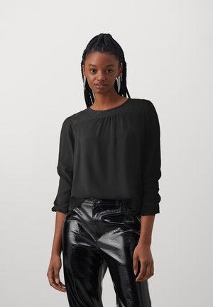Black long-sleeve blouse with lace detail at the neckline, paired with shiny black faux leather pants featuring a textured pattern.