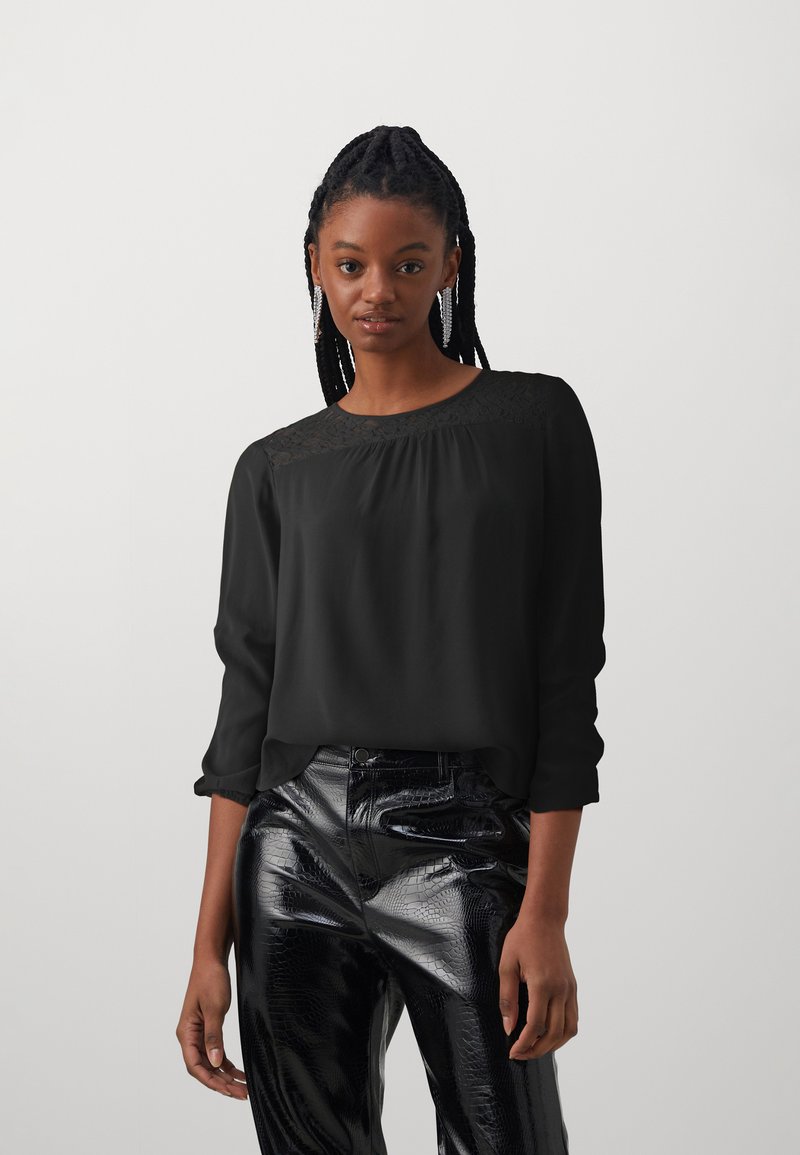 Black long-sleeve blouse with lace detail at the neckline, paired with shiny black faux leather pants featuring a textured pattern.