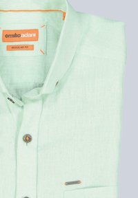 Hellgrünes Leinenhemd, normale Passform, mit spitzem Kragen, orangefarbene Akzente auf dem Etikett und einer Brusttasche mit einem Markierungsetikett.