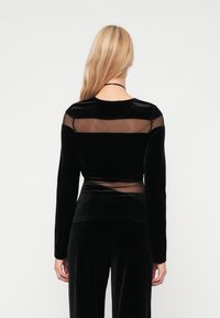 Top de veludo preto de mangas longas com painéis de rede transparentes nos ombros e nas costas. Textura suave, design ajustado e decote arredondado.