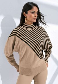 Pullover mit hohem Kragen, diagonalen beige- und schwarzen Streifen, weichem Material und gerippten Bündchen. Begleitet von großen, goldenen Statement-Ohrringen.