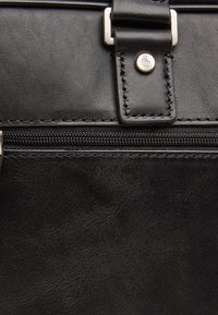 Zwarte leren tas met een ritsluiting. Gladde textuur met een metallic merklogo en vierkante hardware accenten. Gestikte details.