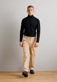 Sort turtleneck, beige bukser og sorte sko. Outfittet har et figursyet design med lange ærmer og en glat tekstur.