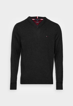 Suéter de manga larga de color gris oscuro con cuello en V, pequeño logo rojo, blanco y azul en el pecho izquierdo, puños y dobladillo acanalados, y cuello interior a rayas.