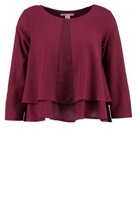 Blouse bordeaux à manches longues avec un design superposé ; le panneau avant présente une texture lisse et unie, avec une couche inférieure légèrement transparente.