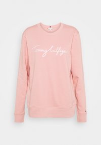 Sudadera rosa hecha de un tejido suave, con cuello redondo, mangas largas y el logo de "Tommy Hilfiger" en cursiva blanca en la parte frontal.