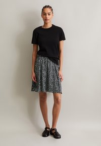 Schwarzes Kurzarm-T-Shirt kombiniert mit einem knielangen, plissierten Rock mit einem schwarz-weißen geometrischen Muster. Getragen mit schwarzen Sandalen.