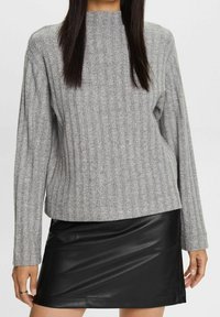 Harmaa ribbattu villatakki pitkillä hihoilla ja korkealla kauluksella, yhdistetty mustaan keinonahkaiseen mini-hameeseen. Pehmeät pinnat ja istuva muotoilu.