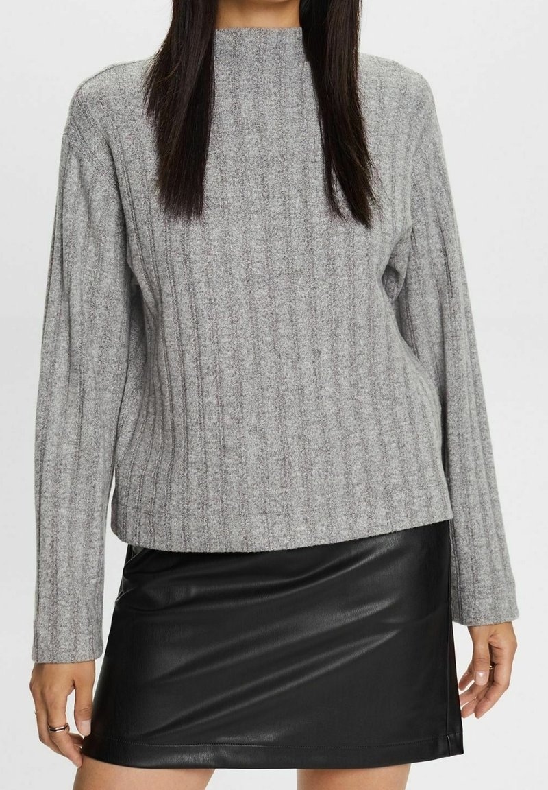 Harmaa ribbattu villatakki pitkillä hihoilla ja korkealla kauluksella, yhdistetty mustaan keinonahkaiseen mini-hameeseen. Pehmeät pinnat ja istuva muotoilu.