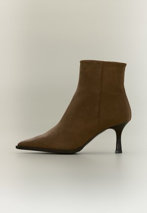 Bottine en daim marron à bout pointu, avec une couture latérale et un talon noir fin, sur un fond clair.