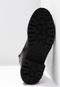 Bottine noire à semelle en caoutchouc texturée. Comprend une fermeture éclair latérale pour un enfilage facile et un détail de couture sur le devant. Taille 37.