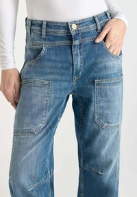 Pantalons cargo en denim bleu avec plusieurs poches à rabat, une fermeture à bouton et une coupe droite avec une finition délavée.