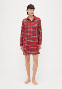Vestito camicia rosso a quadri con maniche lunghe, chiusura a bottoni frontale e tasca sul petto con dettaglio ricamato. Tessuto in cotone con una consistenza soffice.