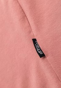 Růžové bavlněné tričko s hladkou texturou a černou etiketou s nápisem "LEVEL UP" na bočním švu. Jednoduchý design a ležérní styl.