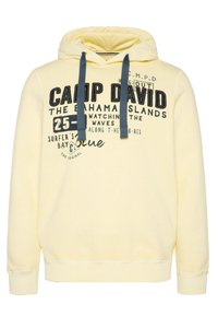 Sudadera amarilla con un gráfico frontal que incluye texto e iconos. Presenta una capucha con cordón y puños y dobladillo acanalados. Textura suave.