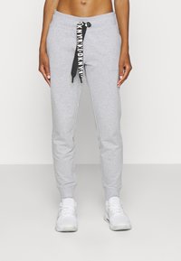 Šedé tepláky z bavlny s pasem na tkaničku, která je černobílá a značková. Na kotnících jsou úzké s žebrovanými manžetami.