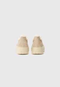 Beige suede shoes with cream fur accents and thick beige rubber soles. Smooth texture on the upper and a sturdy, contoured heel.