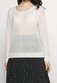 Leichter, transparenter Pullover in Off-White mit lockerer Passform, ausgestattet mit strukturierten Einsätzen und einem weichen Strickfinish. Gerippte Bündchen und Saum.