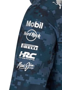 Niebieska kurtka w kamuflażu z różnymi białymi logo, w tym Mobil, Hard Rock, Pirelli, HRC Honda Racing i Maui Jim na rękawie.