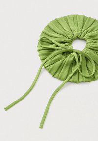 Zelená látková gumička so štruktúrovaným, nazbieraným dizajnom a dvoma dlhými šnúrkami vyčnievajúcimi z okrajov.