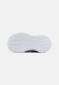 Suela de una zapatilla; goma blanca texturizada con un agarre en patrón; material superior negro liso visible en los bordes.