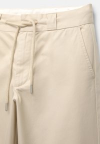 Beige bomuldsblandede bukser med snøre i taljen, forreste lommer og glat tekstur. Inkluderer hardware i sølvtoner.